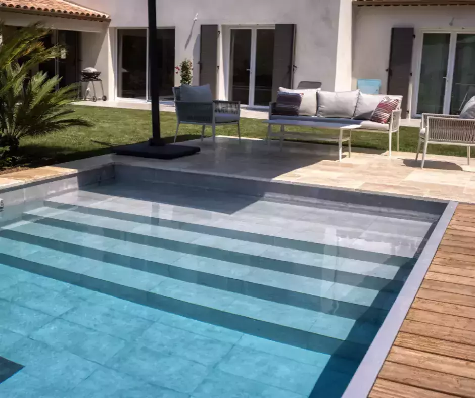 une piscine rectangulaire avec couloir de nage, terrasse aménagée en trois espaces, et végétation évoquant le littoral.