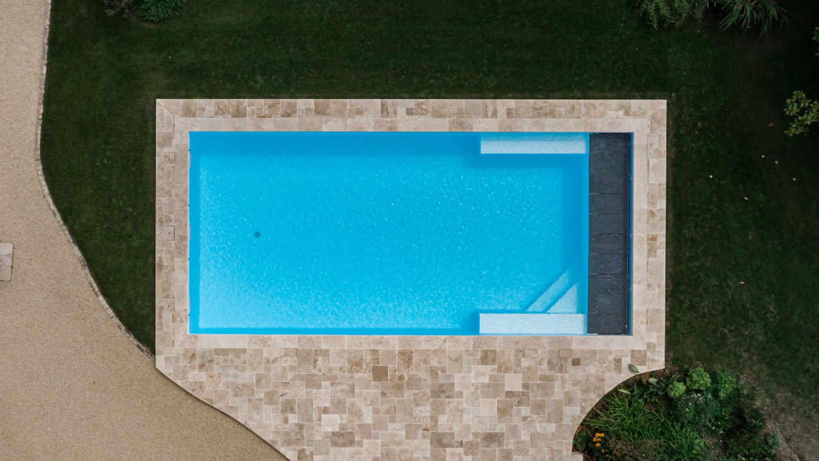 Cette vue dépeint une piscine dont le blanc du liner offre une eau d'apparence paradisiaque.