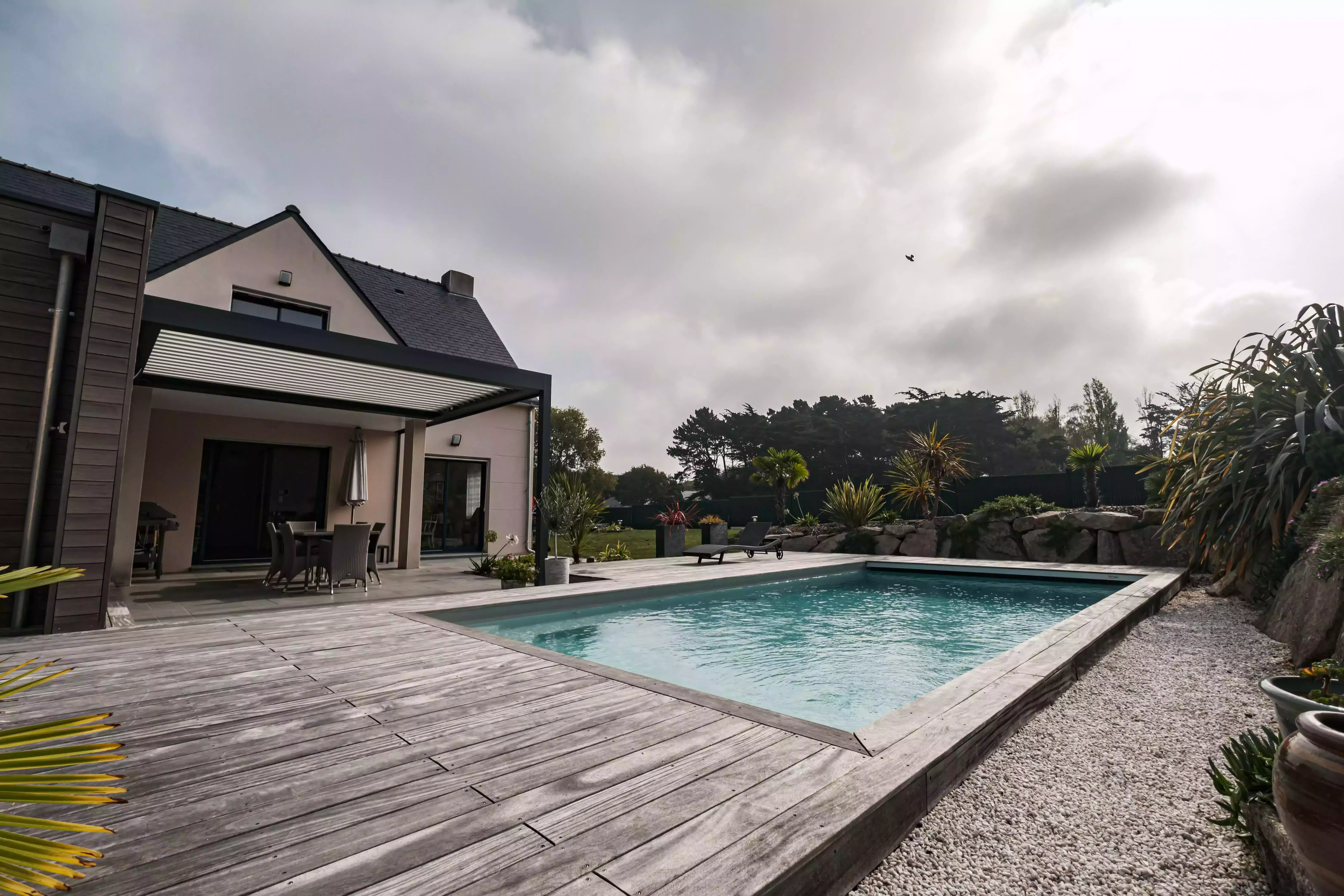 Une architecture moderne qui priorise la piscine, unie à un décor rocheux grâce à une terrasse, le tout agrémenté de verdure exotique.