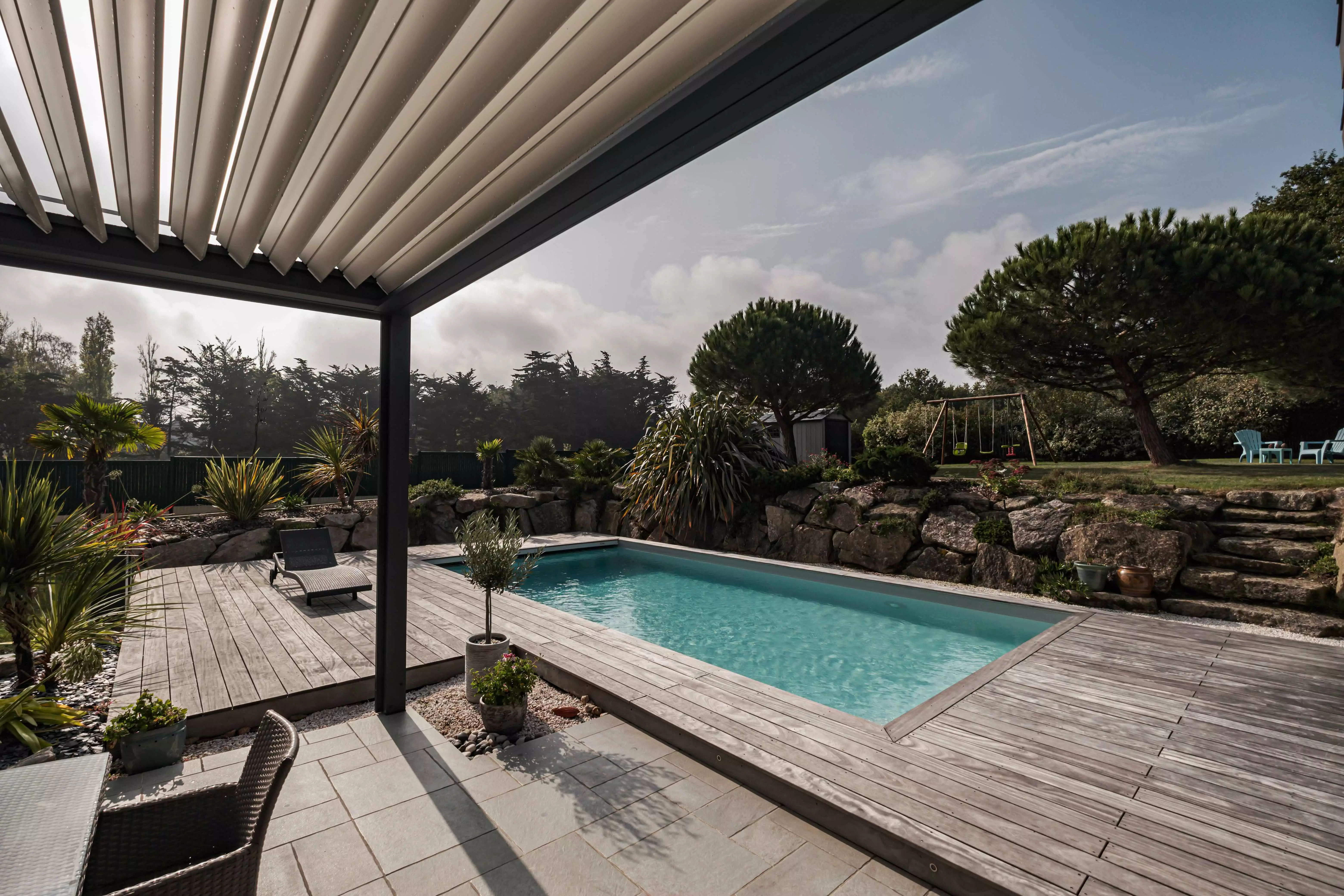Une demeure moderne avec la piscine en vedette, bordée d'une terrasse qui s'étend vers un paysage rocheux enrichi de plantes exotiques.