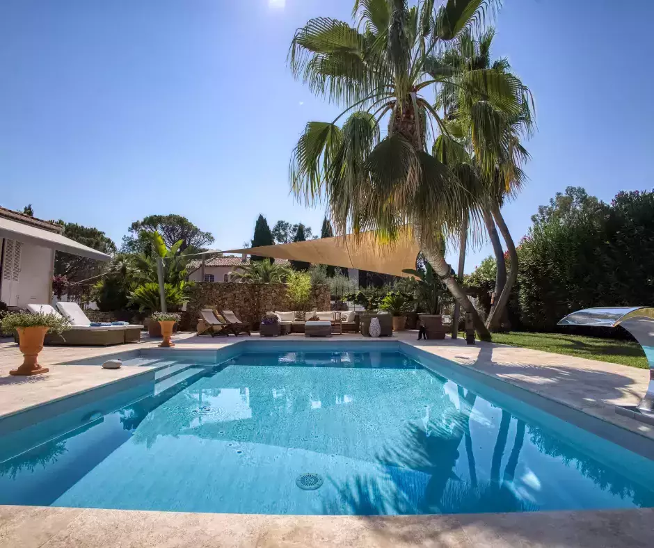 Réaménagement d'une piscine en coque en une élégante piscine en maçonnerie, rehaussée par un palmier spectaculaire, un jeu d'eau et un espace détente en travertin.